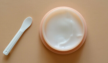 Plastic jar of beauty cream or mask for face care with spatula on pastel background. Concept of skincare cosmetic, cosmetic spa medical skin care. 