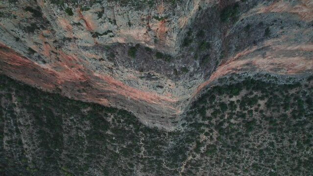 Drone top down descends across intimidating sheer cliff face with dry shrub landscape, tilt up pullback to leonidio greece