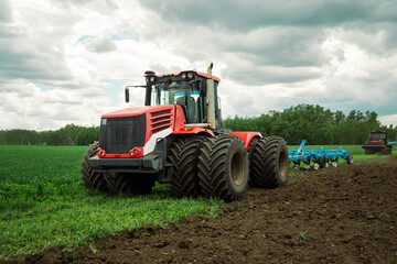 Obraz premium Red tractor working in a field on a bright sunny day. The concept of work in a fields and agriculture industry.