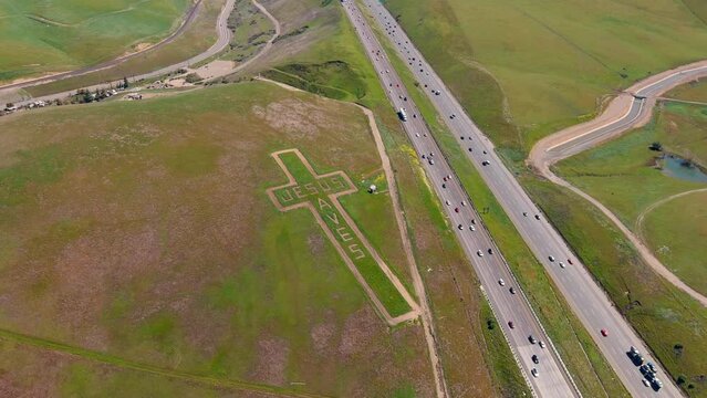 "Jesus Saves" mowed into the grass on a hill, Cross on the Hill at Altamont Pass, aerial