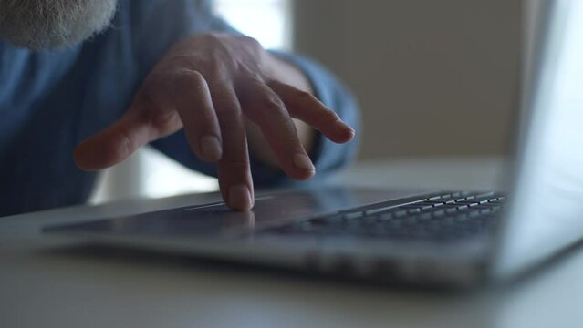 Close-up cropped shot of unrecognizable mature adult wrinkled fingers touching and sliding on touchpad of laptop. Closeup of senior businessman working at notebook outdoors. Shooting in slow motion.