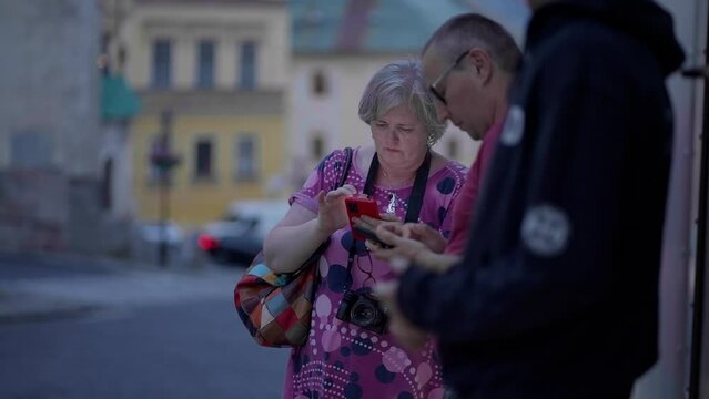 Tourists - Man and a Woman looking at their phones for directions in a historical European town Banska Stiavnica surrounded by historical buildings during a blue hour at dusk. 4K, Sony FX3