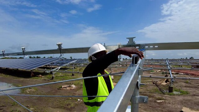 Black Gambian African male engineer man taking solar energy farm panel array frame tilt angle slope measurement using a digital protractor at a photovoltaic power plant in Gambia, West Africa