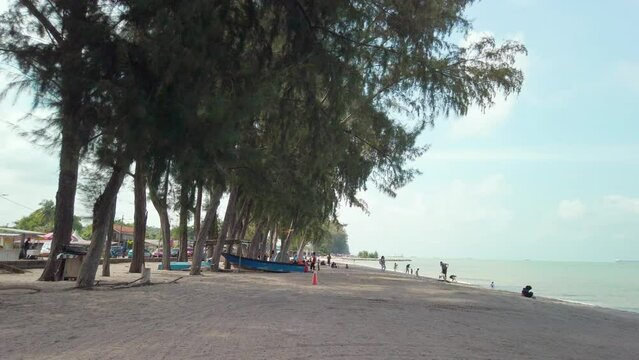 Cinematic footage of Pantai Puteri Beach in Melaka, Malaysia, during a partly cloudy day. People are seen enjoying the shoreline, having picnics, and having fun.
