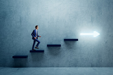 Side view of young businessman climbing illuminated arrow stairs to success on concrete wall...