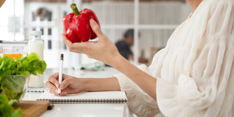Keto diet concept. Happy asian woman writing daily ration diet or menu in notebook, sitting near various products at kitchen table, free space