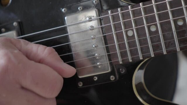 A close-up image of a guitarist's right hand picking the strings on a black 
335 style electric guitar.