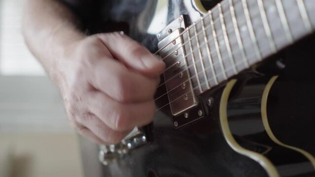 Close-up, side view of a guitarist's right hand playing rhythm on an electric guitar.