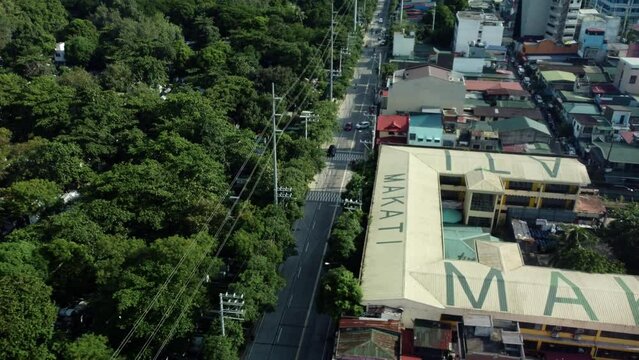 Drone shot of Philippine road next to cemetery full of trees and school with Makati written on top