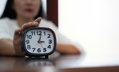 Female hand turning off black and white alarm clock at workplace.