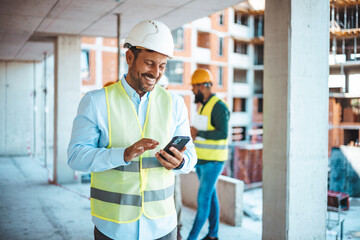 Businessman using his smartphone while on a construction site. Portrait of young engineer in vest...