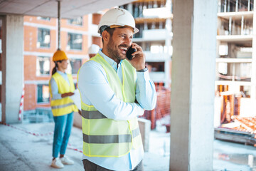 Fototapeta na wymiar Smiling architect in suit and with helmet on head standing in building in construction process. Repair, building, construction, business and maintenance concept. Smiling man in helmet 