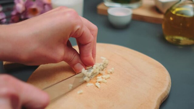 Female hands finely chop garlic on the kitchen table. Close-up of the table. Cooking in the kitchen