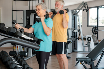 Fototapeta na wymiar Athletic senior couple keeping fit working out together in the gym doing dumbbell lifting exercise. Sports life as a retiree