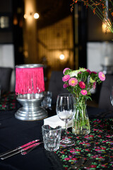 Glasses, flowers, fork, flowers, knife served for dinner in restaurant with cozy interior
