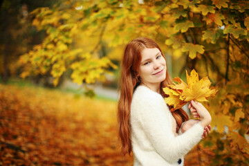 Naklejka na ściany i meble Autumn leaves falling on happy young girl in forest. The colors and mood of autumn. 