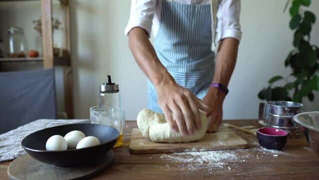 A baker in an apron kneads the dough with his hands and sprinkles it with flour to bake delicious homemade tortillas