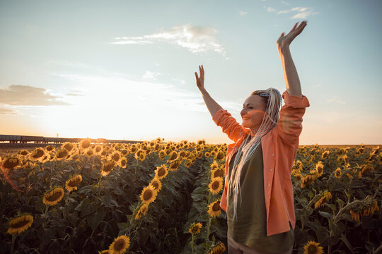 Smiling woman with arms raised standing in sunflower field