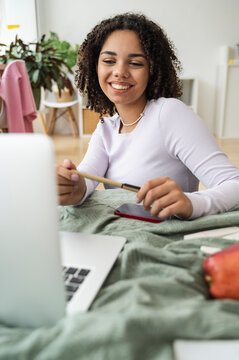 Happy teenage girl talking on video call through laptop in bedroom at home