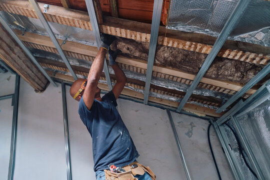 Construction worker installing insulation on ceiling in attic