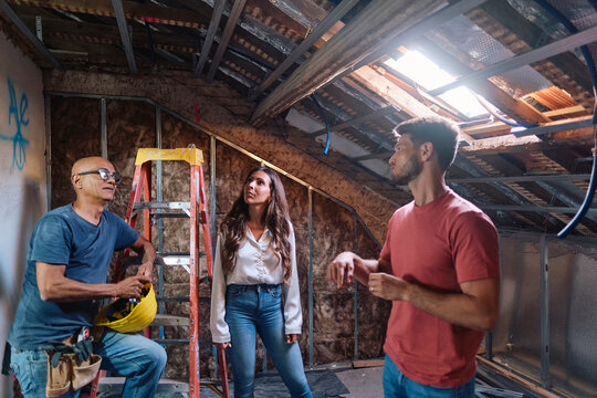 Man and woman having discussion with construction worker in attic at home