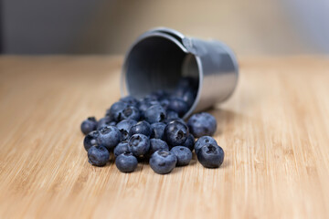 Scattered blueberries in a bucket on a wooden board