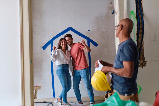 Construction worker with couple cheering in front of wall at site