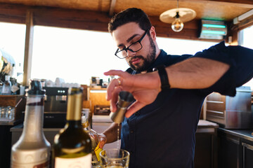 Young bartender wearing eyeglasses preparing drink in cafe