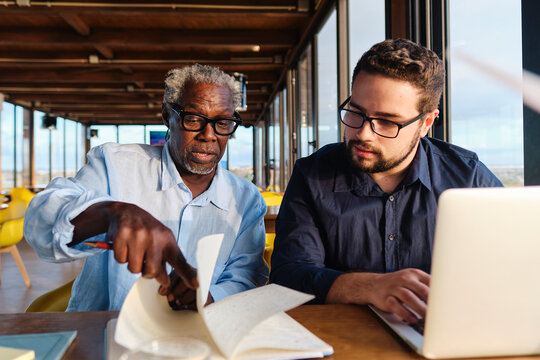 Senior engineer explaining and having discussion over diary with colleague in cafe