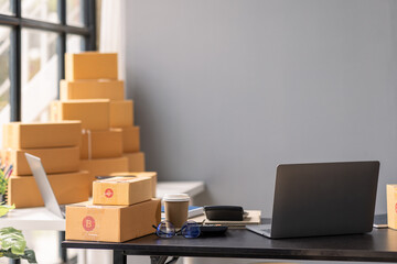 Parcel boxes on shelf and color shopping bags placing near laptop on table. SME business on shopping online at home office packaging on background is popular business.
