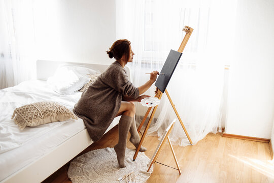 Woman painting on canvas in bedroom at home