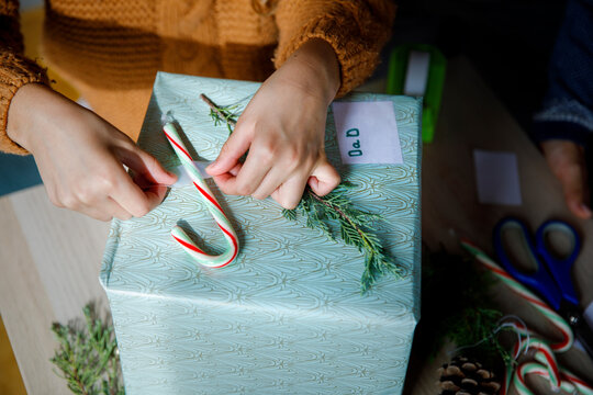 Girl sticking candy cane on gift box at home