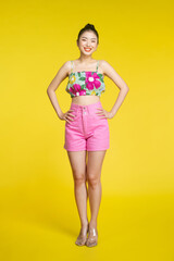 Young asian woman isolated on yellow background posing with arms at hip and smiling