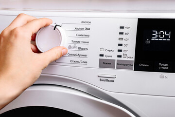 Woman select program at modern automatic washing machine. Laundry and housework concept.