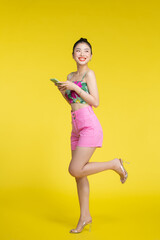 Fototapeta na wymiar Beautiful Asian woman holding smartphone and smiling on light yellow background