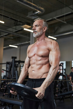 Shirtless mature man doing strengthening exercise with weight plate