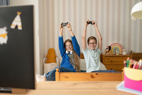 Cheerful girl and boy playing video game together at home