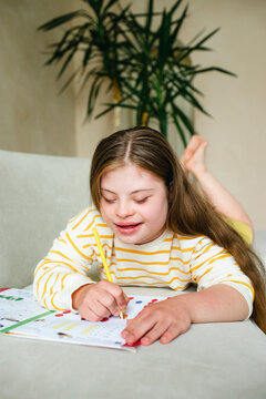 Smiling girl with down syndrome writing in workbook at home