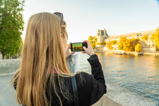 Blond tourist taking photo of Seine river through smart phone