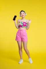 Asian pretty woman wearing headphones and holding on her cell phone over yellow background.