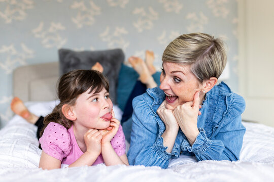 Cheerful mother and daughter making facial expression lying on bed