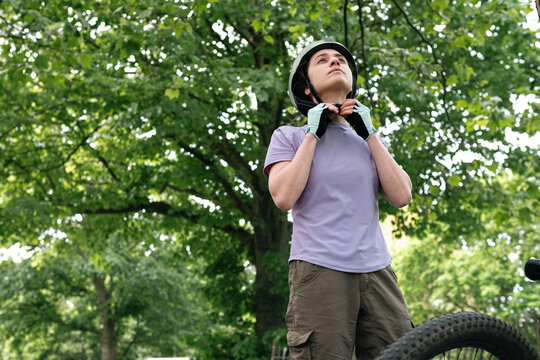 Woman fastening helmet under tree at forest