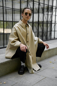 Young man wearing sunglasses sitting in front of modern building
