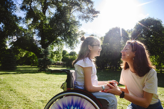 Smiling daughter in wheelchair talking with mother at park