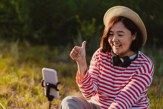 Happy mature woman gesturing thumbs up and vlogging on mobile phone