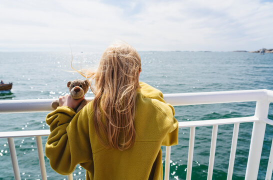 Blond girl with teddy bear near railing in ferry moving on sea