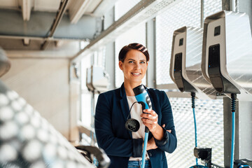 Smiling businesswoman with electric plug at charging station