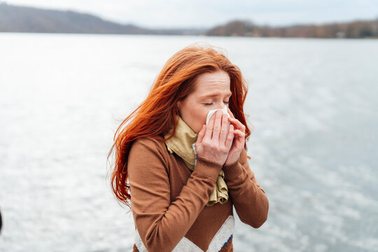 Redhead woman blowing nose in front of lake