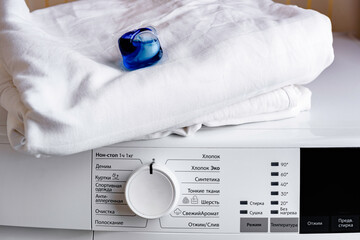 Woman putting laundry detergent capsule with white clothes into washing machine. 