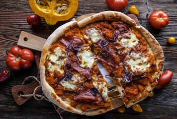 Homemade pizza with pumkin sauce, tomatoes, red onions, italian salami and mozzarella cheese